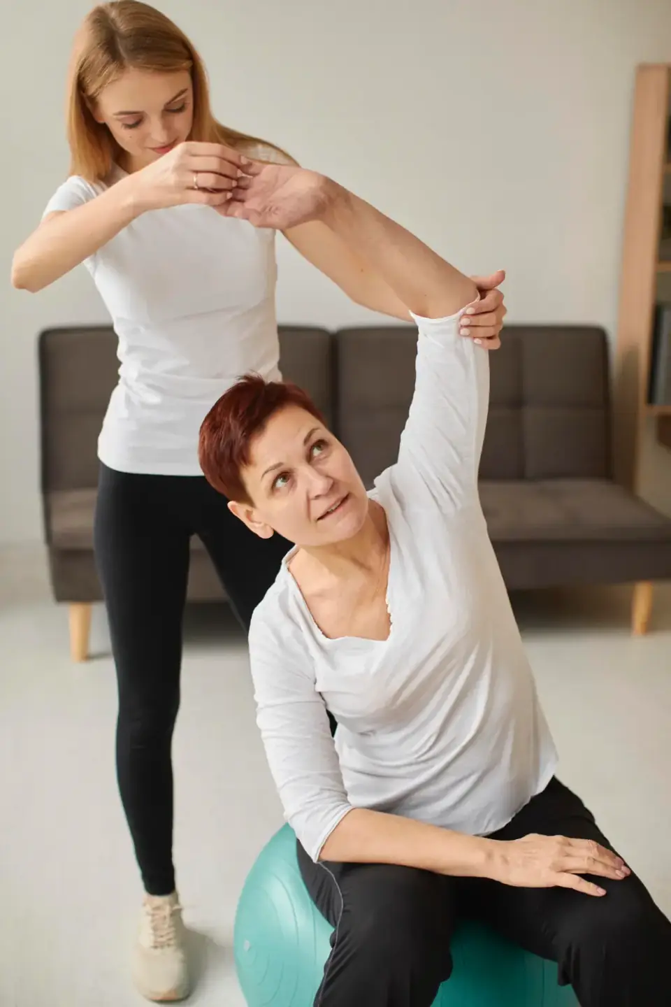 Therapeutin unterstützt eine ältere Patientin bei einer Übung auf dem Gymnastikball